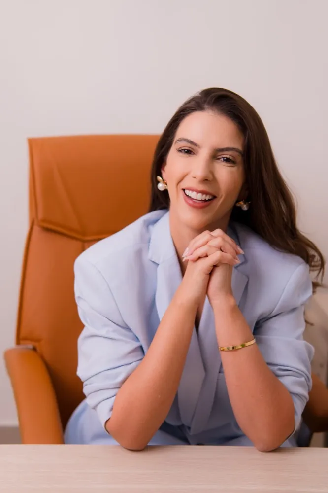 Dra. Kattia Rogério sorrindo, sentada na poltrona do consultório